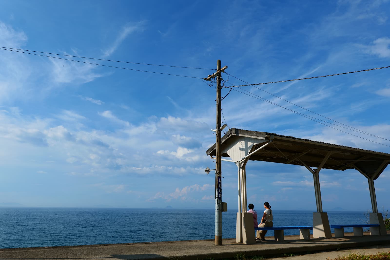 海が見える小さな駅のホームでベンチに座る人の様子