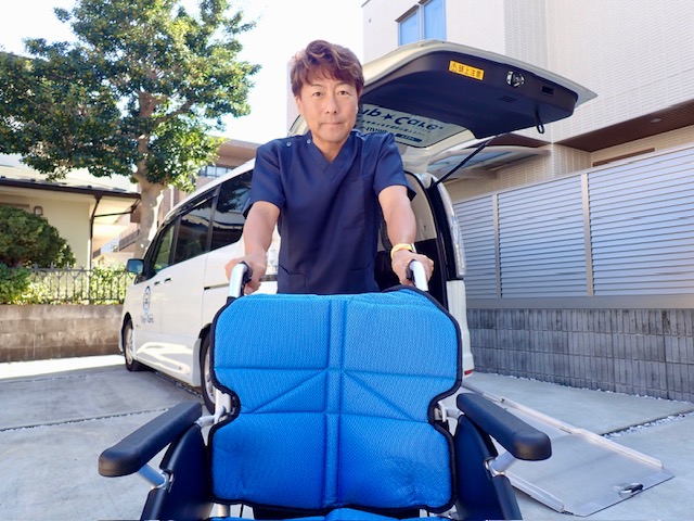福祉介護車両をバックにグループ会社であるスタッフが車いすを押す様子