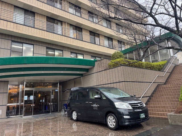 雨の日の乗降時に濡れないようエントランス屋根下に福祉介護タクシー車両を止める様子